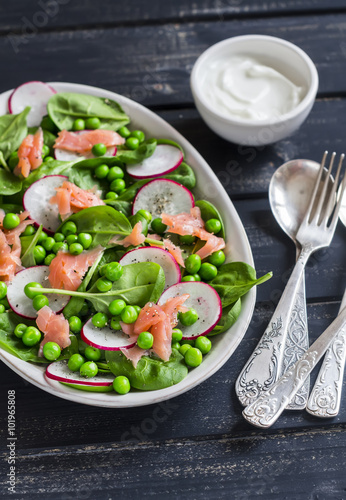 Fresh salad with green peas, spinach, radish and smoked salmon on a ceramic plate on a dark wooden background