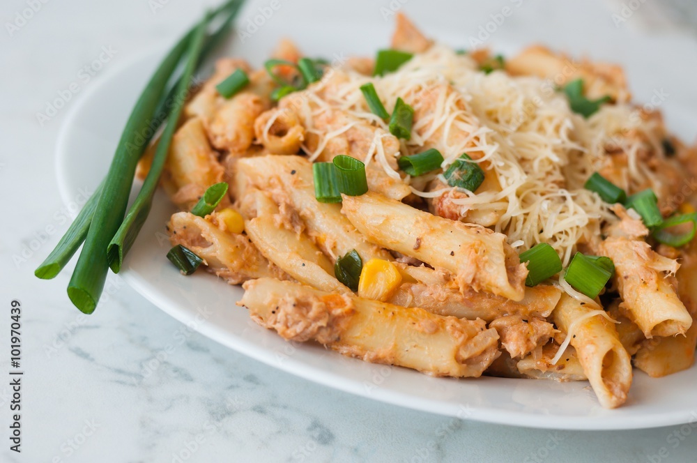 Penne pasta with healthy tuna fish, cheese and chopped scallion or spring onion leaves. Served on a white oval plate
