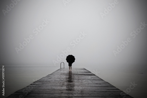 elegant woman dressed in black hiding with umbrella in a misty l