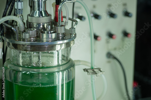 Close up of large glass beaker with green fluid, tubing and metallic parts for lab