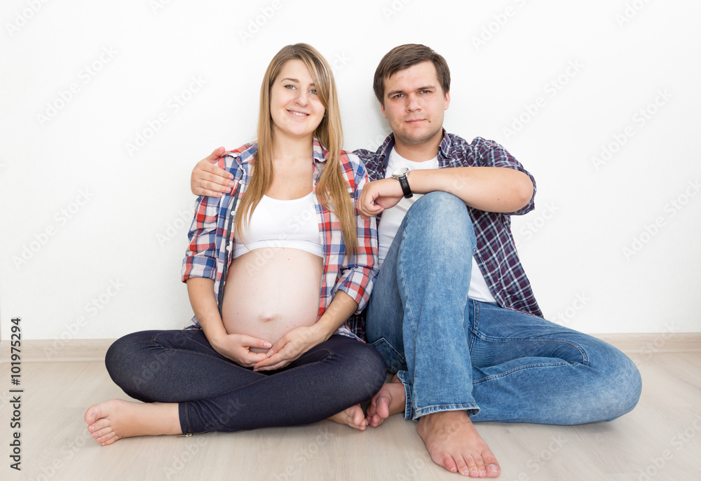 pregnant couple in jeans and shirts sitting on floor at empty ro pregnant couple in jeans and shirts sitting on floor at empty ro