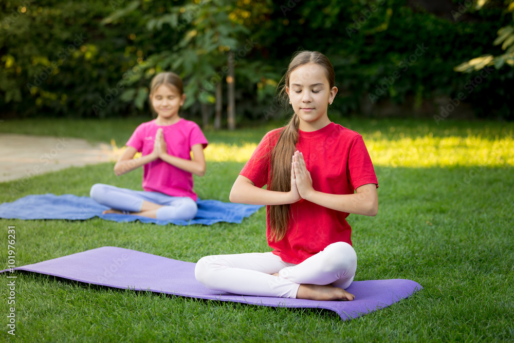 Two smiling sisters practicing yoga on grass at park Two smiling sisters practicing yoga on grass at park
