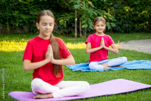Two cute girls practicing yoga at park at sunny day