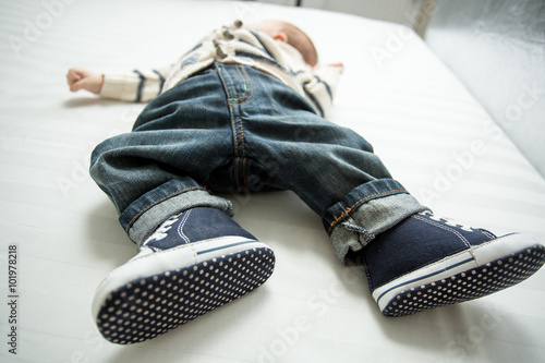 Closeup of baby boy feet in jeans and sneakers lying on bed