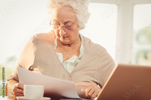 Senior woman dealing with documents while using laptop