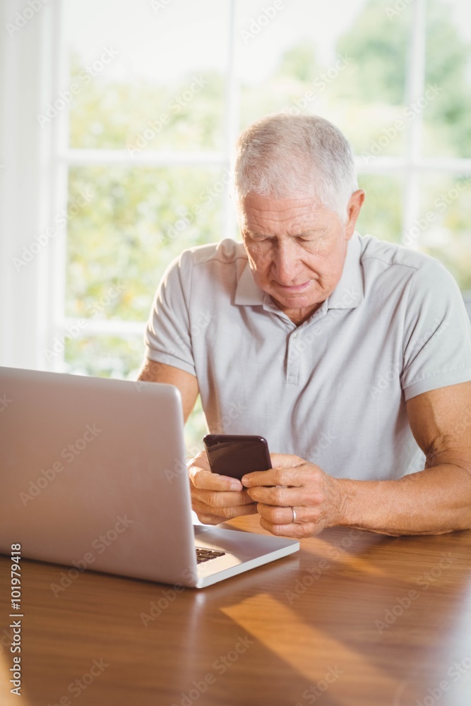 Focused elderly man using smartphone and laptop Focused elderly man using smartphone and laptop