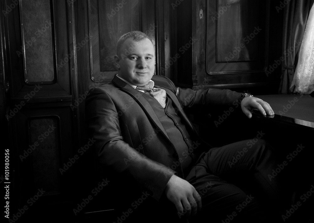 portrait of stylish man in retro suit sitting in armchair at off