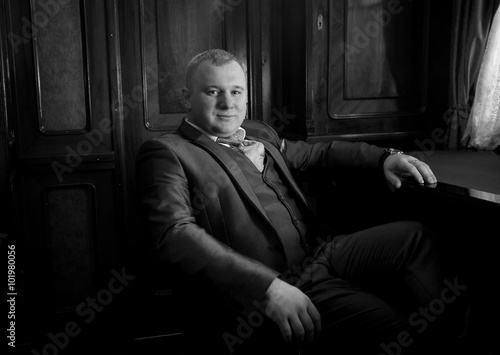 portrait of stylish man in retro suit sitting in armchair at off