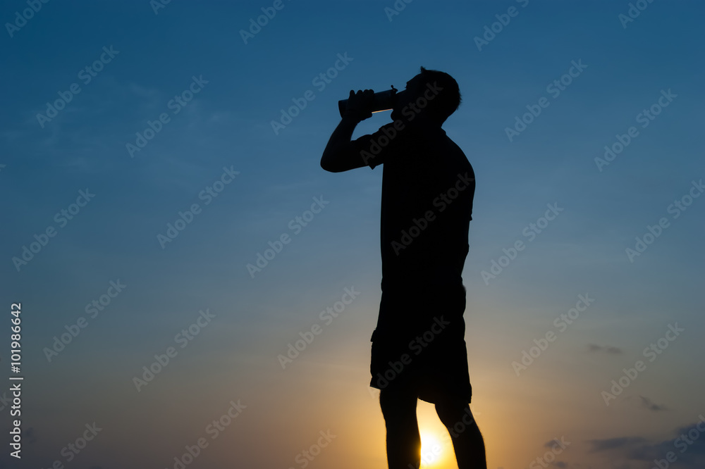 The man drinks from a bottle at dawn