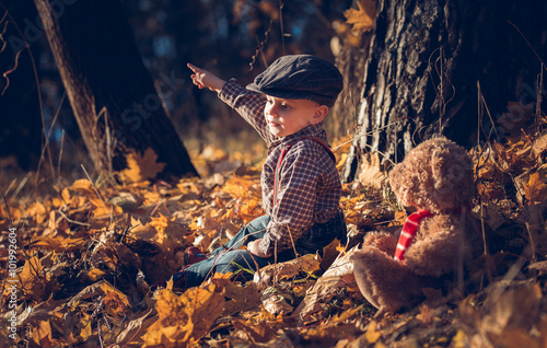 Boy playing outdoor with his teddy bear in autumnal scenery