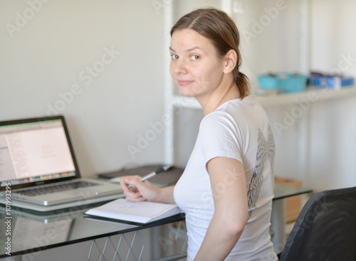 The girl in a white shirt sits at a table with a computer.