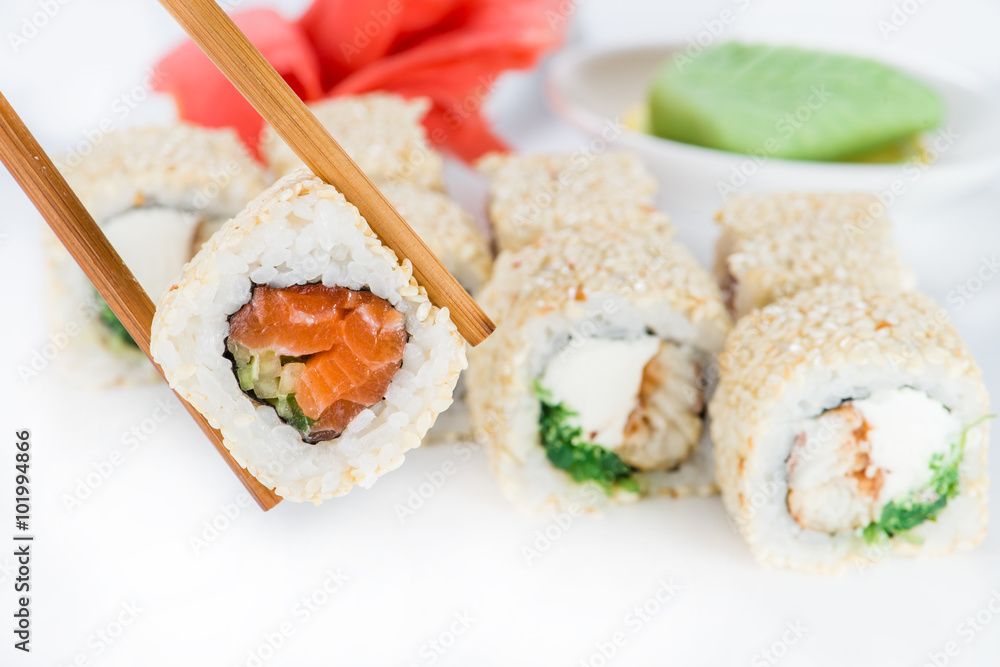 close up of chopsticks taking portion of sushi roll on the table close up of chopsticks taking portion of sushi roll on the table