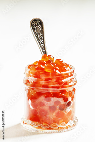 Red salmon caviar in a glass jar on a white wooden background, s