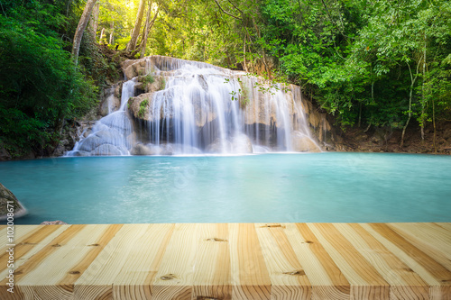 Waterfall  green forest in Erawan National Park in Thailand montage with wooden floor. Landscape with water flow  tree  river  stream and rock at outdoor. Beautiful scenery of nature for vacation.