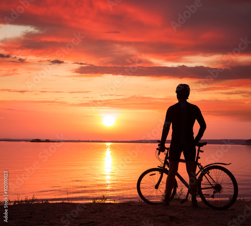 Man Standing with a Bike at Sunset © Maryia Bahutskaya