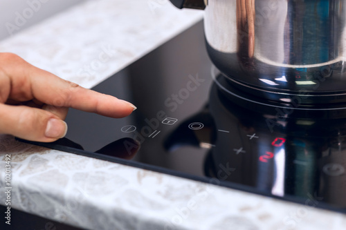 Bild auf Leinwand Woman hand turns on modern induction kitchen