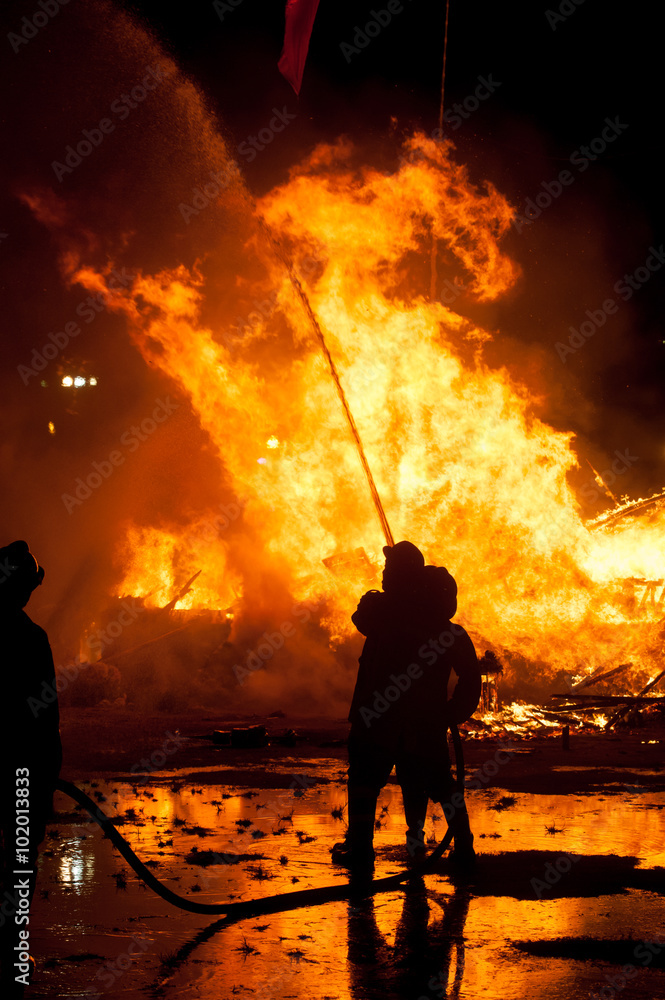 Fototapeta premium Silhouette of Firemen fighting a raging fire with huge flames of burning timber