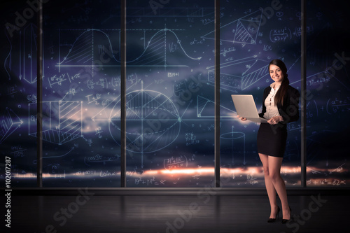 Businesswoman holding laptop in office room with graph charts on