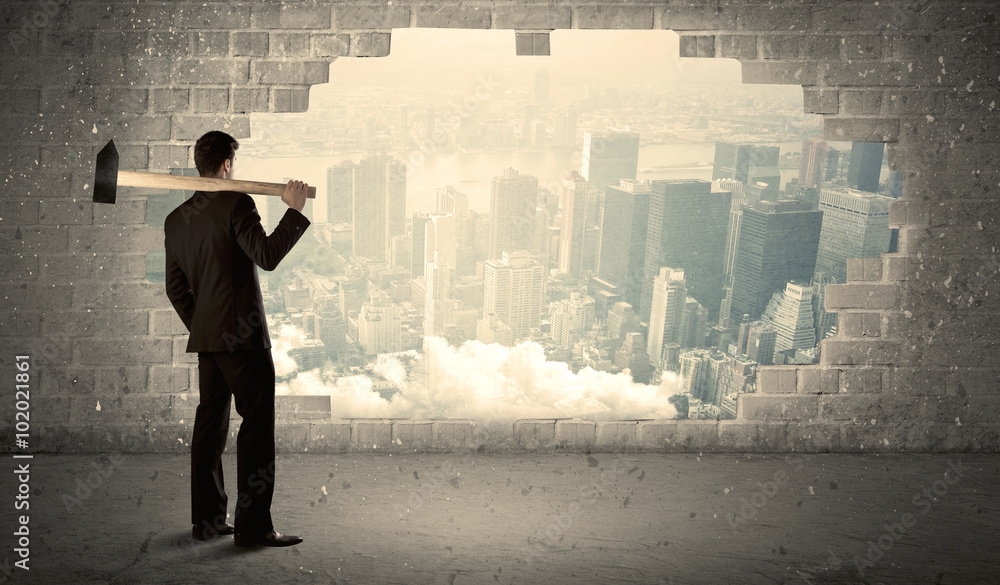 © ra2 studio - Business man hitting wall with hammer on city view