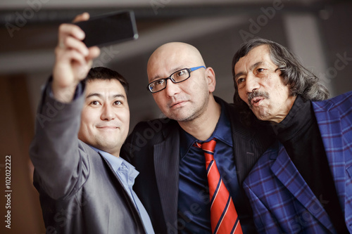Businessmen in suits doing selfie indoors, mature. Business team of three people. Modern technology, social networking, profile picture.