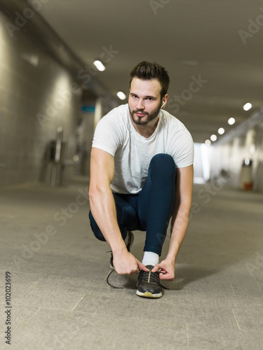 Urban jogger tying his running shoes on a big bridge.