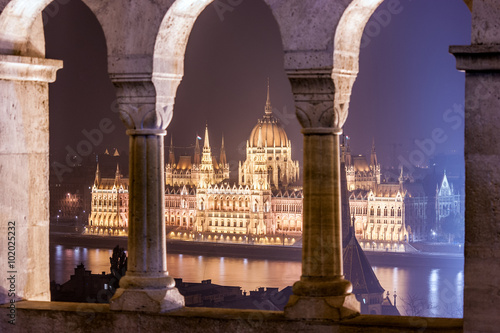 Obraz na plátně Night view of the Hungarian Parliament Building between the columns of the fortr
