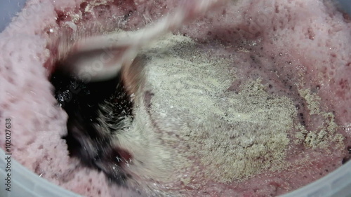 Stirring dried brewer's yeast and yeast nutrient into the grape juice and water mixture of a homebrew wine kit. 