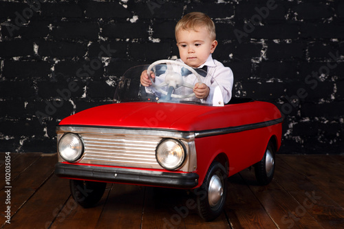 Foto Little boy plays with big red toy car, black background