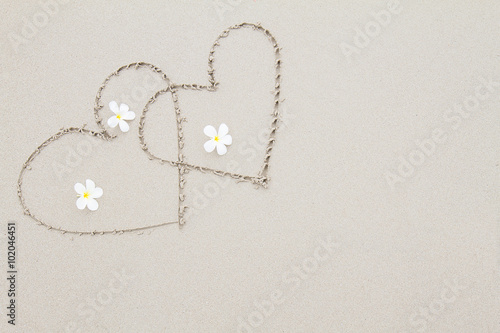Two hearts with white flowers on the beach surface background