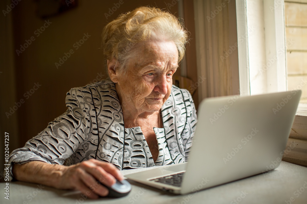 Elderly woman working on laptop at home sitting at the table. Elderly woman working on laptop at home sitting at the table.