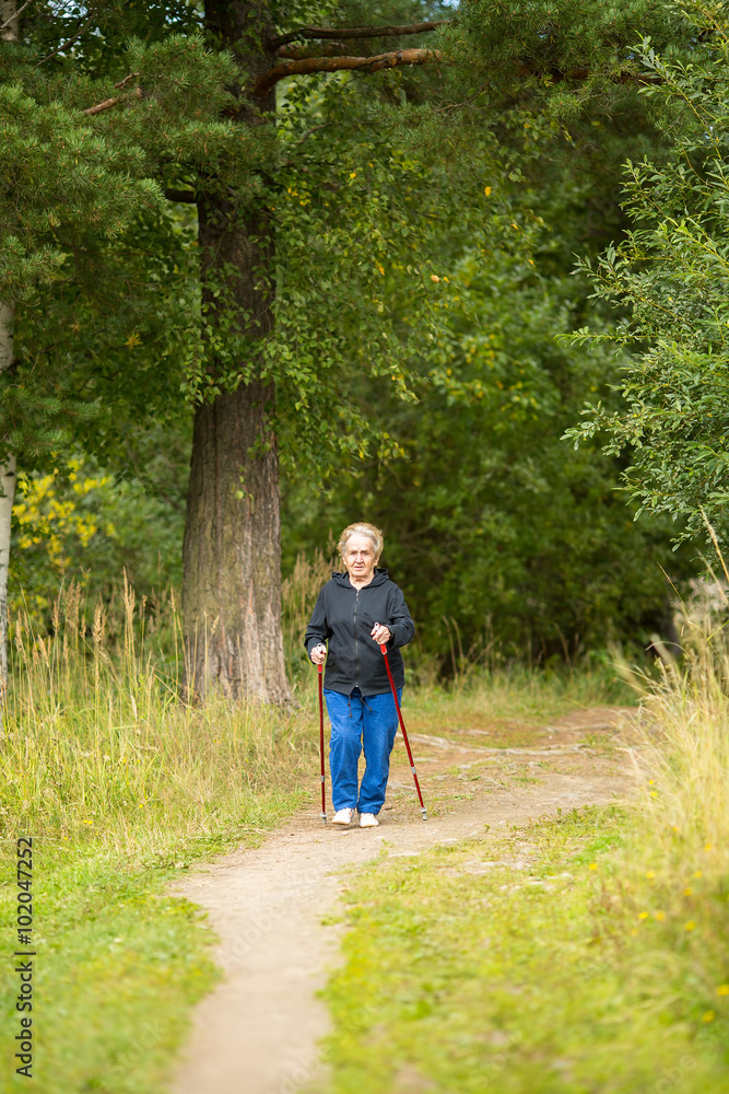 Fototapeta premium An elderly woman on a walk in the Park practicing Nordic walking.