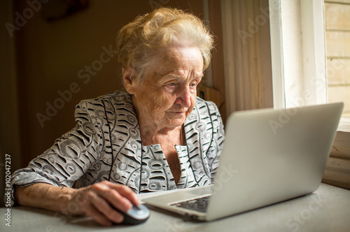 Elderly woman working on laptop at home sitting at the table.