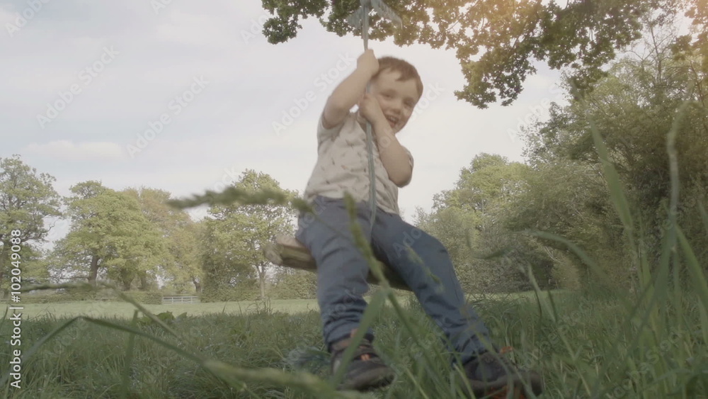 A little boy is playing on a rope swing in a rural field. His legs brush past long grass as he has fun swinging. Shot in the UK and filmed in slow motion at 240fps. A little boy is playing on a rope swing in a rural field. His legs brush past long grass as he has fun swinging. Shot in the UK and filmed in slow motion at 240fps.