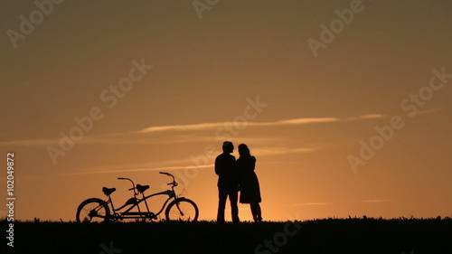 Silhouette of  Romantic Couple With Tandem Bicycles Watching And Enjoyig The Sunset  Leaning Together photo