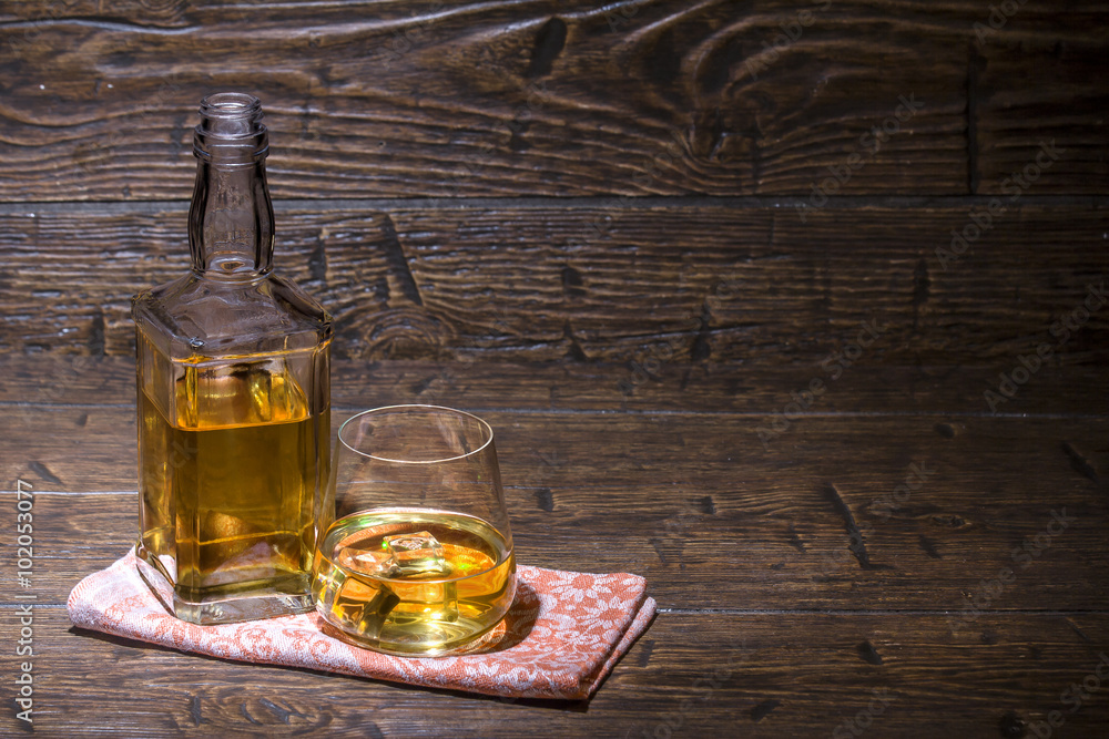 Bottle and a glass with whiskey and ice are on the napkin Bottle and a glass with whiskey and ice are on the napkin