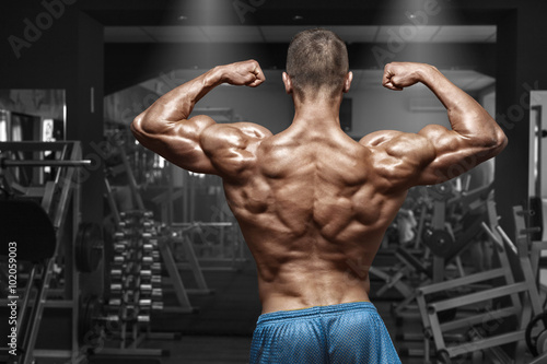 Rear view muscular man posing in gym  showing back and biceps. Strong male naked torso  working out