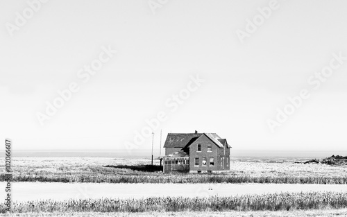 Abandoned two level brick house with broken windows in a rural black and white countryside landscape photo