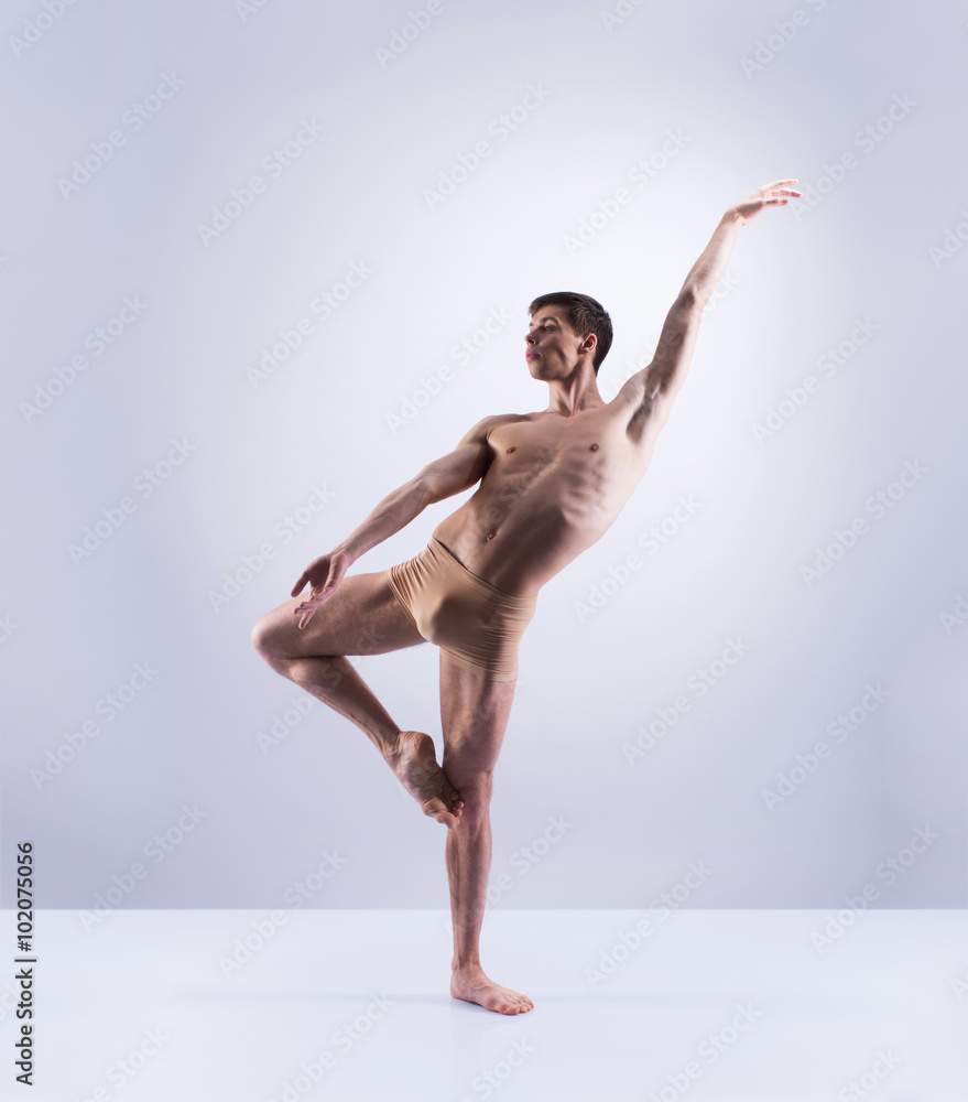 Fototapeta premium Athletic ballet dancer in a perfect shape performing over the grey background.