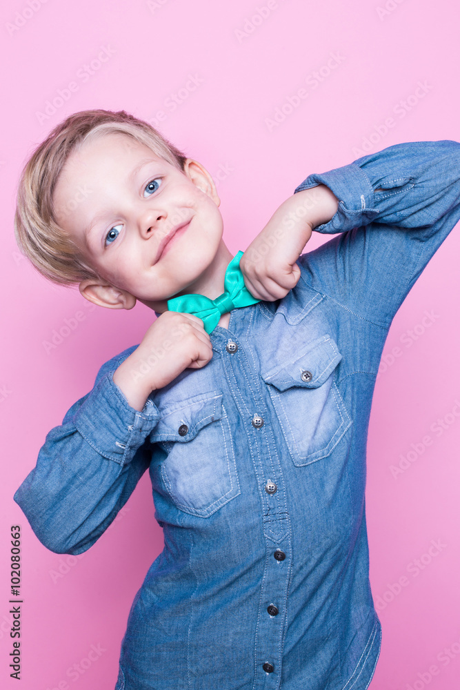 Young beautiful boy with blue shirt and butterfly tie. Studio portrait over pink background Young beautiful boy with blue shirt and butterfly tie. Studio portrait over pink background