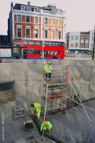 Scene from Finsbury Park, London with red bus and people in uniforms at work using scaffolding photo