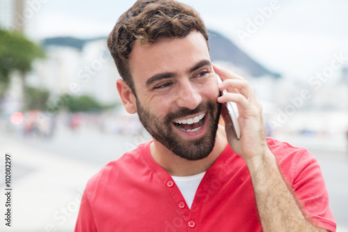 Fröhlicher Mann mit Bart im roten Shirt am Telefon