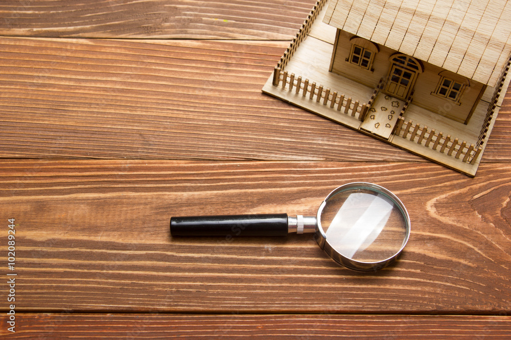 Fototapeta premium Real Estate Concept. Model house and magnifying glass on wooden table. Top view.