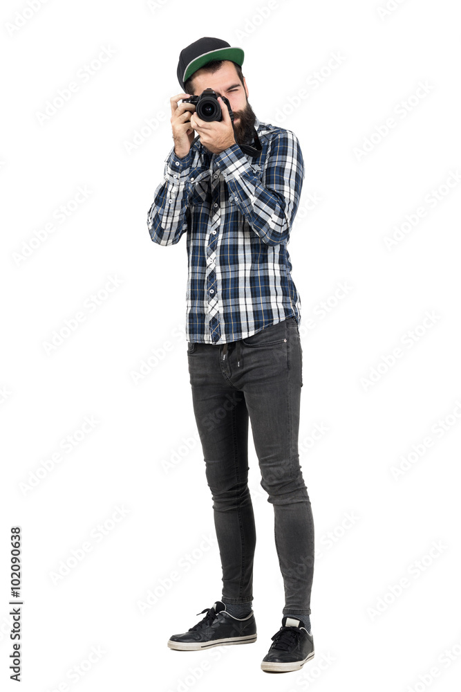 Hipster in plaid shirt taking photo with dslr camera looking at camera. Full body length portrait isolated over white studio background. Hipster in plaid shirt taking photo with dslr camera looking at camera. Full body length portrait isolated over white studio background.