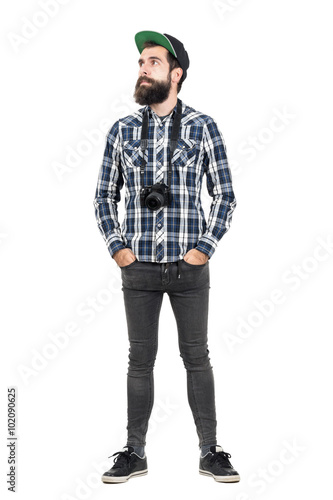 Relaxed hipster wearing black dslr camera over neck with hands in pockets. Full body length portrait isolated over white studio background. © sharplaninac
