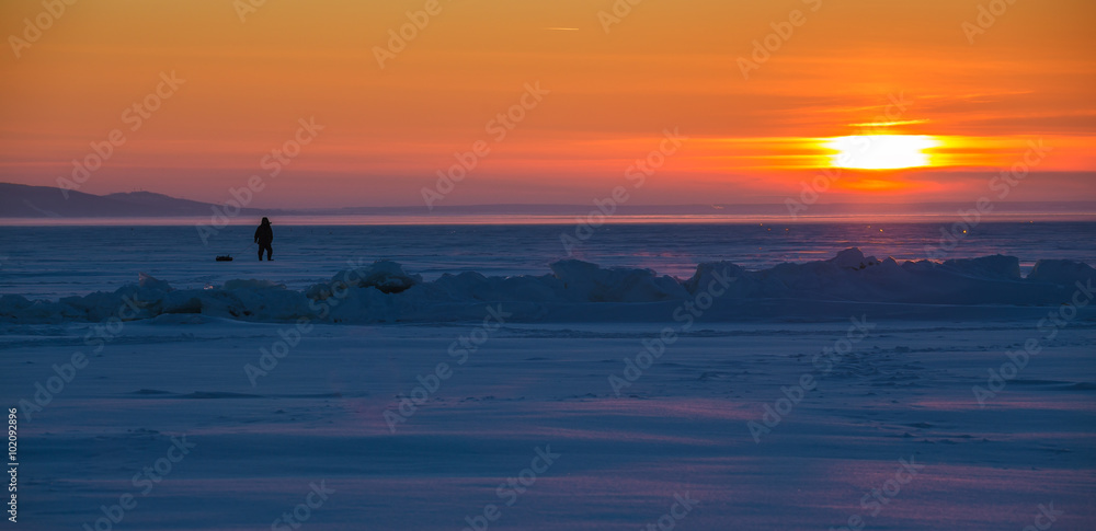 fisherman on the ice of the river at sunset