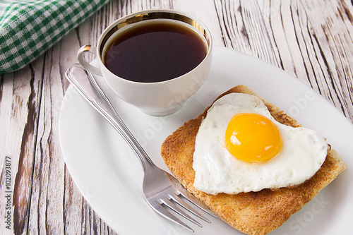 Fried egg on bread for breakfast on plate with a cup of coffee and rustic table