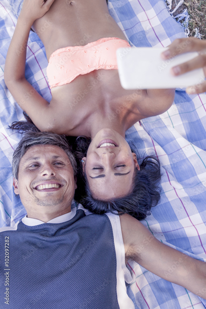 Fototapeta premium young couple lying on cloth take a selfie lying in the park