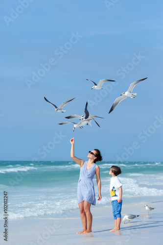 Young mother and her little son feeding seagulls on tropical beach, Florida