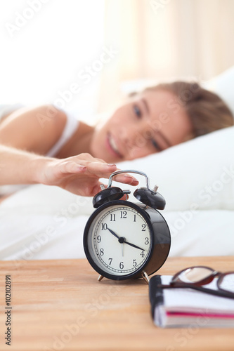 Young sleeping woman and alarm clock in bedroom at home