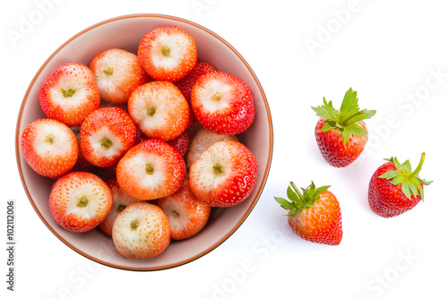 Red ripe strwberries in a bowl with few on white table photo